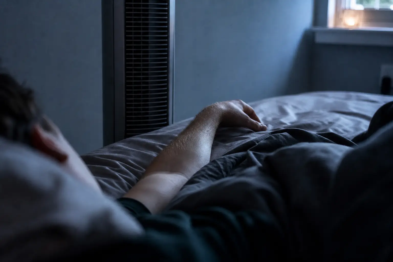 Turmventilator neben einem Bett und einem nackten Unterarm